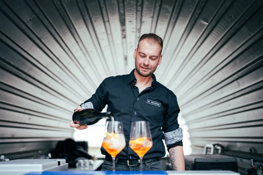 Barman dolévá nápoj do dvou sklenic s pomerančem.