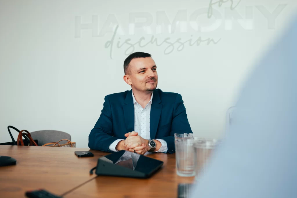 Muž v modrém saku sedí za konferenčním stolem s tabletem.