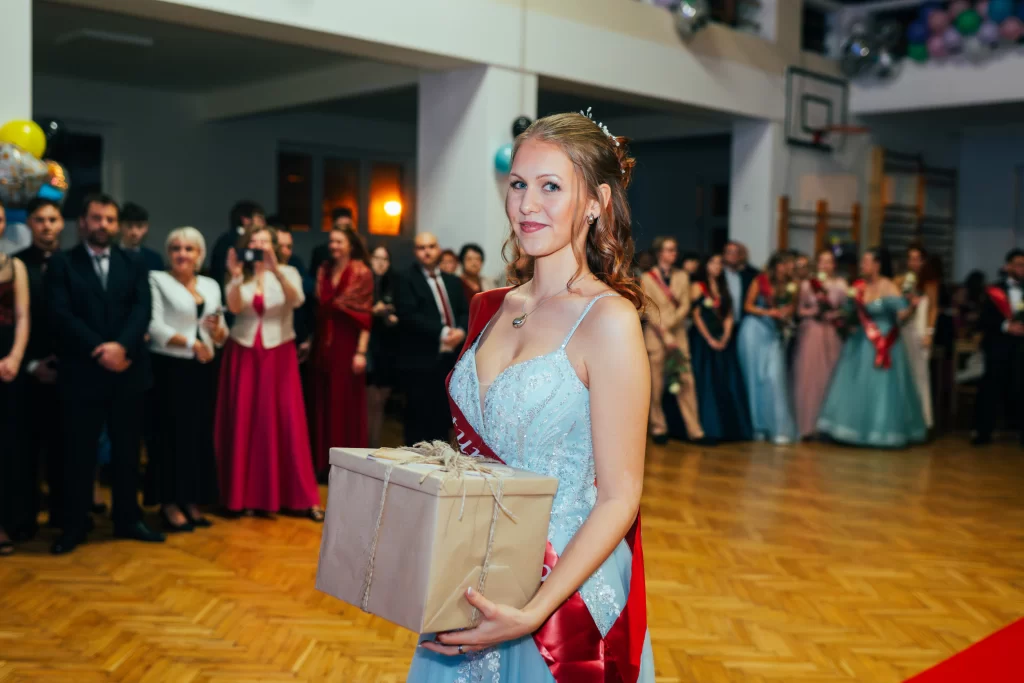 Maturantka ve světle modrých šatech nese zabalený dárek.