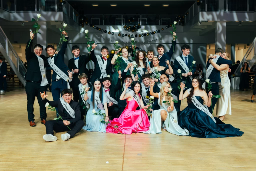 Společný portrét maturantů ve společenských šatech a oblecích na parketu.