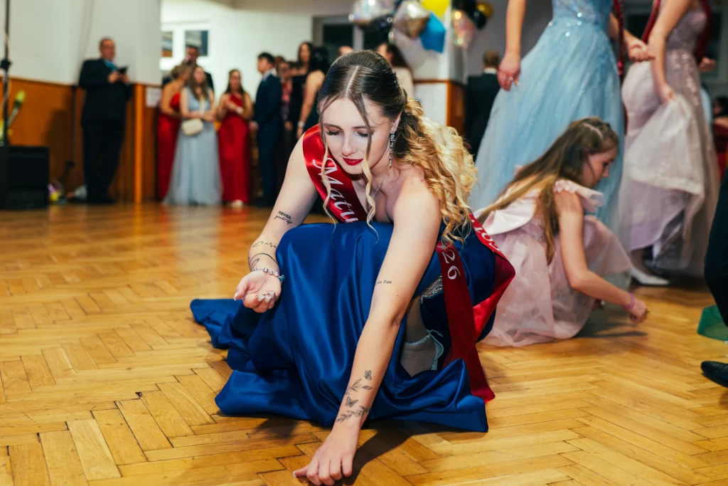 Maturantka v modrých šatech klečí na parketu při sbírání mincí.