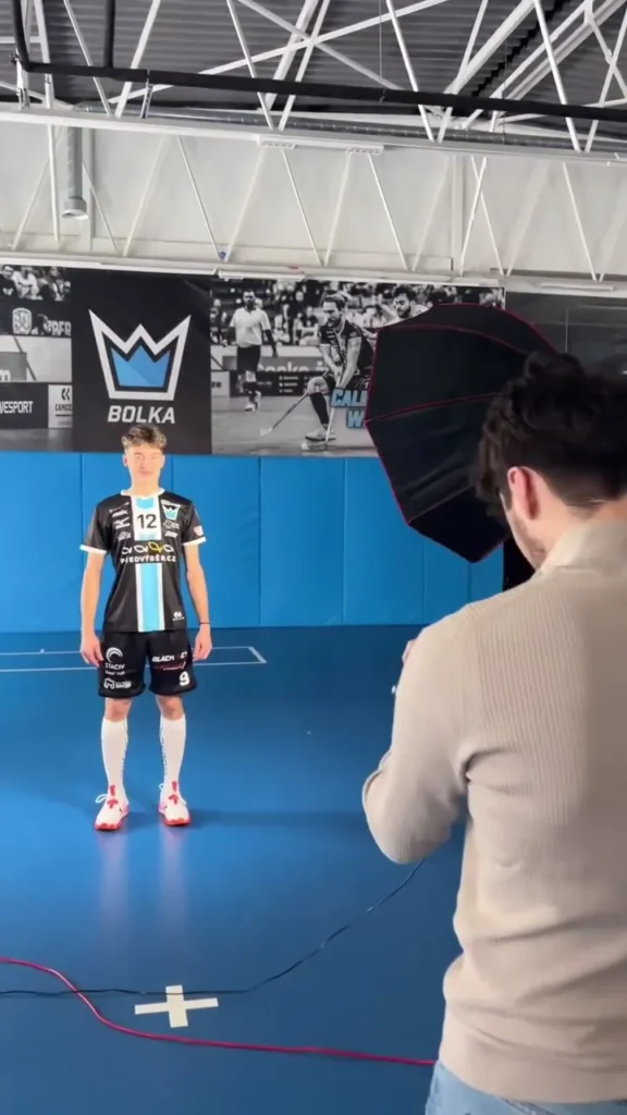 Fotograf při focení florbalisty v modré sportovní hale.