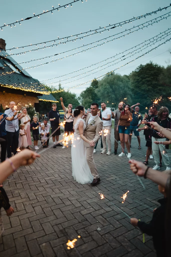 Nevěsta se ženichem procházejí mezi hosty držícími prskavky.